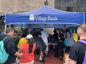 Group of people waiting to get their haircut under a Village Bank tent.